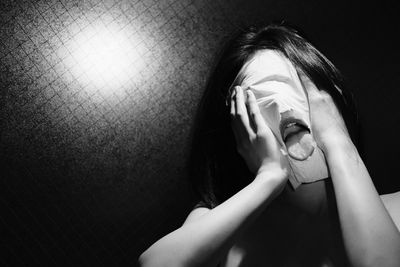 Close-up portrait of woman covering face against wall