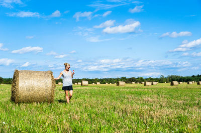 Woman standing by hay bale on field against sky