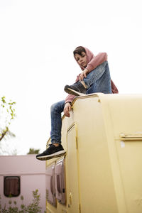 Low view of a young boy sitting on the top of a caravan