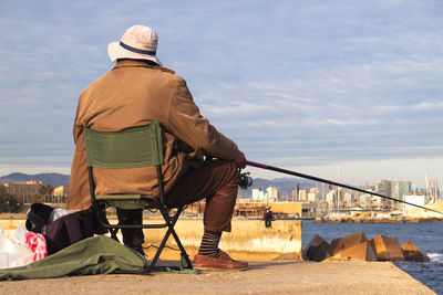 Rear view of man fishing at harbor against sky
