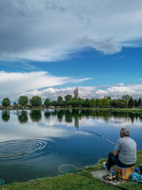 Rear view of man on bicycle by lake against sky