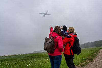 Two women with a child in their arms watch airplanes