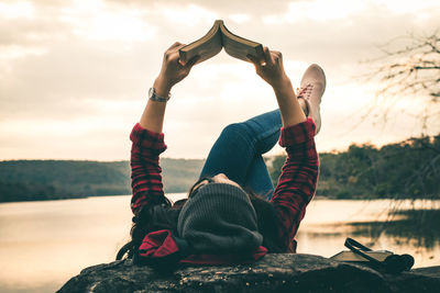 Woman reading book while lying on lakeshore during sunset