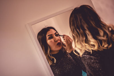 Rear view of woman applying make-up in front of mirror