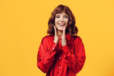 Portrait of young woman standing against yellow background