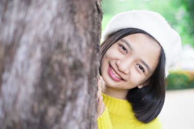 Portrait of smiling young woman against tree trunk