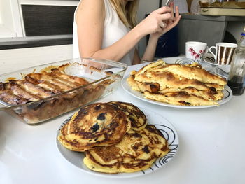 Midsection of woman using phone while having pancakes on table