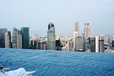 Low section of man resting by swimming pool at marina bay sands against city