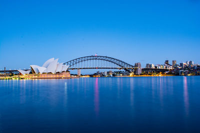 Illuminated ferris wheel in front of sea against clear blue sky