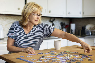 Woman playing jigsaw puzzle at table in home