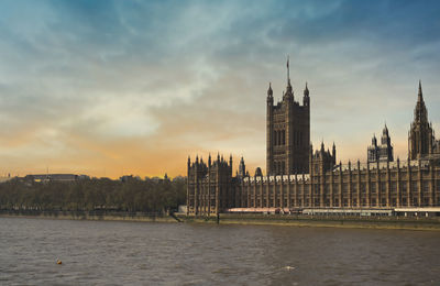 Buildings at waterfront against cloudy sky