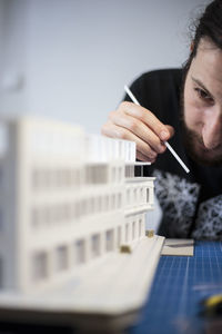 Young man preparing architectural model on table