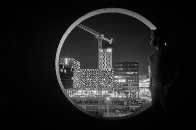 Man looking at illuminated cityscape through window