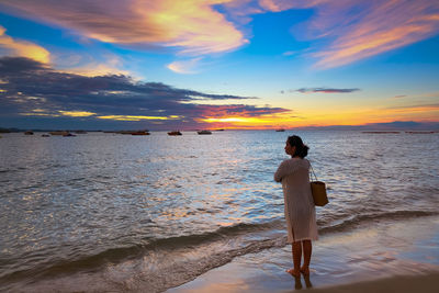 Rear view of woman standing on beach during sunset