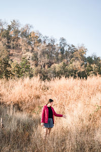 Woman standing in meadow against forest