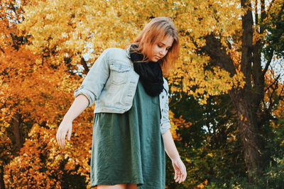 Portrait of smiling young woman standing by tree during autumn