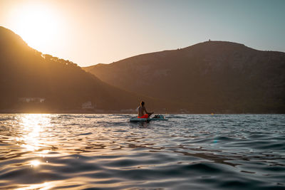 Man sitting on boat in lake against sky during sunset