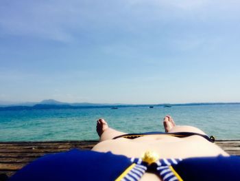 Low section of young woman in bikini resting on pier by sea