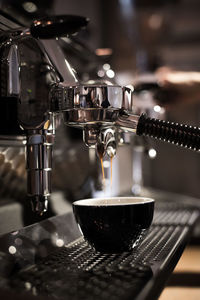 Close-up of machinery dripping coffee in cup at cafe