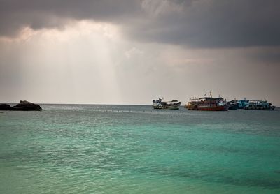 Boats sailing in sea against cloudy sky