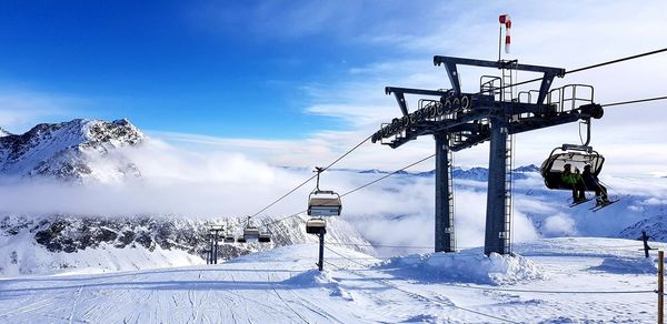 Ski lift over snow covered mountains against sky