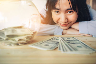 Close-up portrait of smiling young woman with paper currency on table