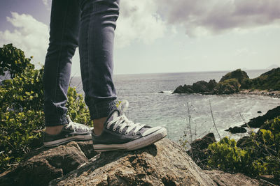 Low section of person on rock by sea against sky