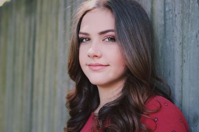 Portrait of young woman with brown wavy hair against wall