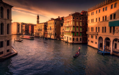 Canal amidst buildings in city against sky during sunset