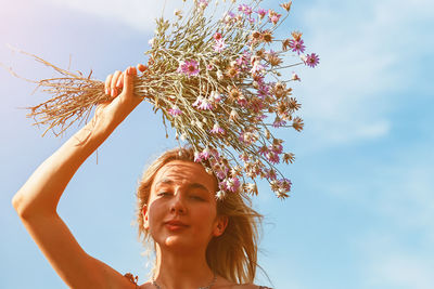 Young beautiful woman smiling to the sun holding a bouquet of wildflowers above her head