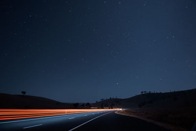 Light trails on road against sky at night