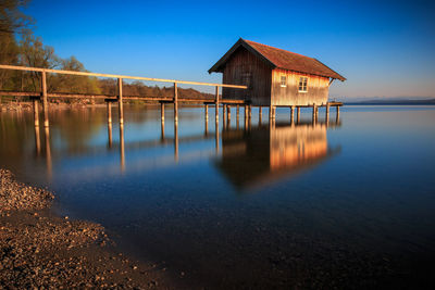 Wooden house by lake against clear blue sky