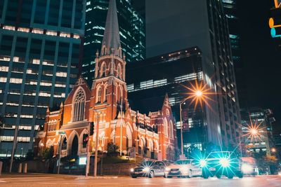 Illuminated city street by church and buildings at night