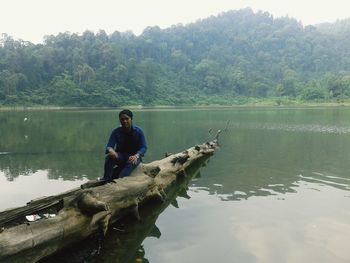 Man sitting on lake against trees