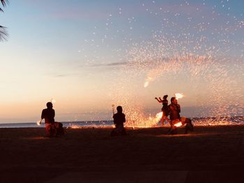 Fire dancers on beach against sky during sunset