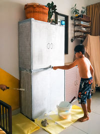 Shirtless boy painting cabinet at home