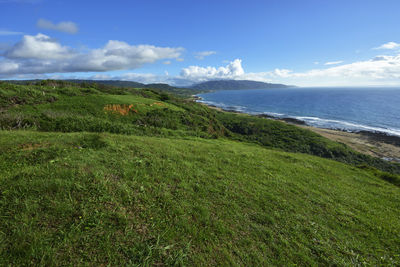 Scenic view of green landscape and sea against sky