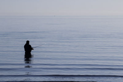 Silhouette man fishing in sea against sky