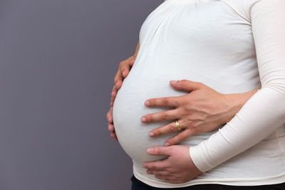 Midsection of woman touching face against gray background