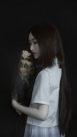 Portrait of young woman standing against black background