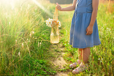 Little girl in blue dress, holding a knitted bag with a bouquet of daisies 