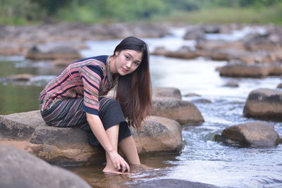Young woman sitting on rock by stream