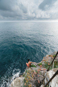 High angle view of man on rock over sea against sky