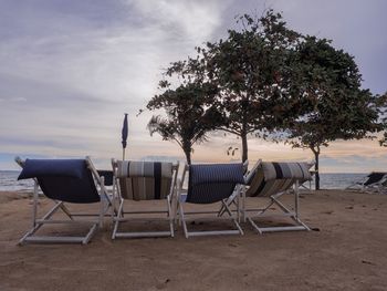 Empty chairs and table on beach against sky