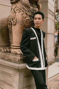 Portrait of young woman standing against building