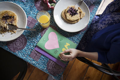 Overhead view of woman eating pancakes by greeting cards on table on birthday