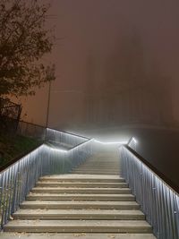 Empty footpath by illuminated wall at night