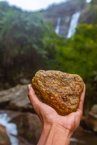 Human hand holding rock against river water and stones