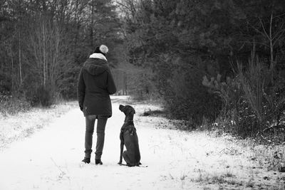 Rear view of woman with dog standing on snow covered road