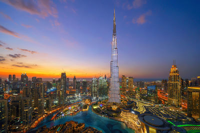 Illuminated city buildings against sky during sunset